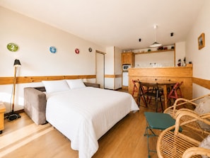 Una habitación con cama, escritorio, silla, lámpara y kitchenette.