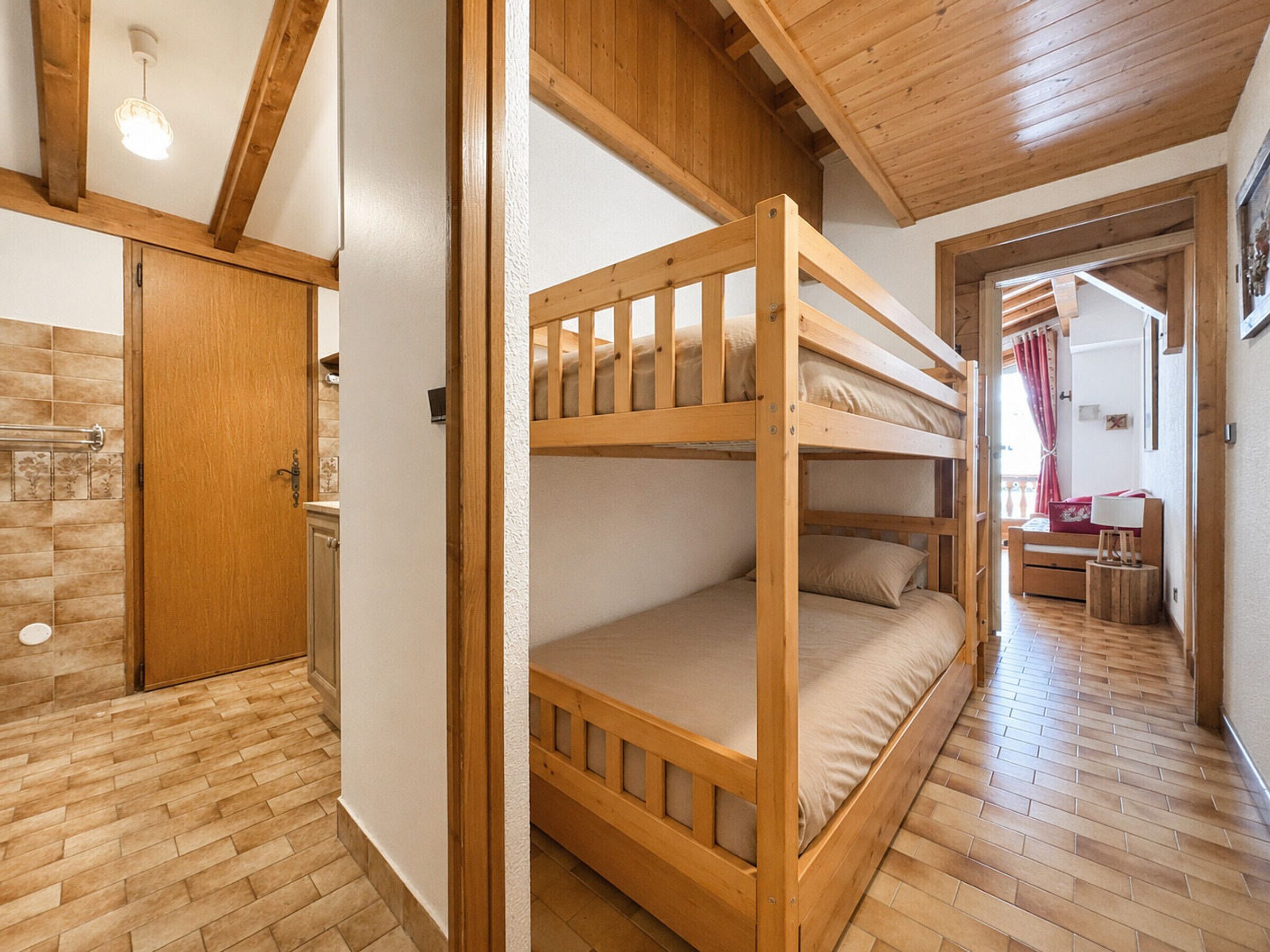 Habitació amb un llit superposat, sòl de fusta, una porta i un passadís que condueix a una altra habitació.