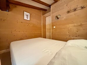 A wooden-paneled room with a bed, a framed picture of a cat, and a heart-shaped mirror.