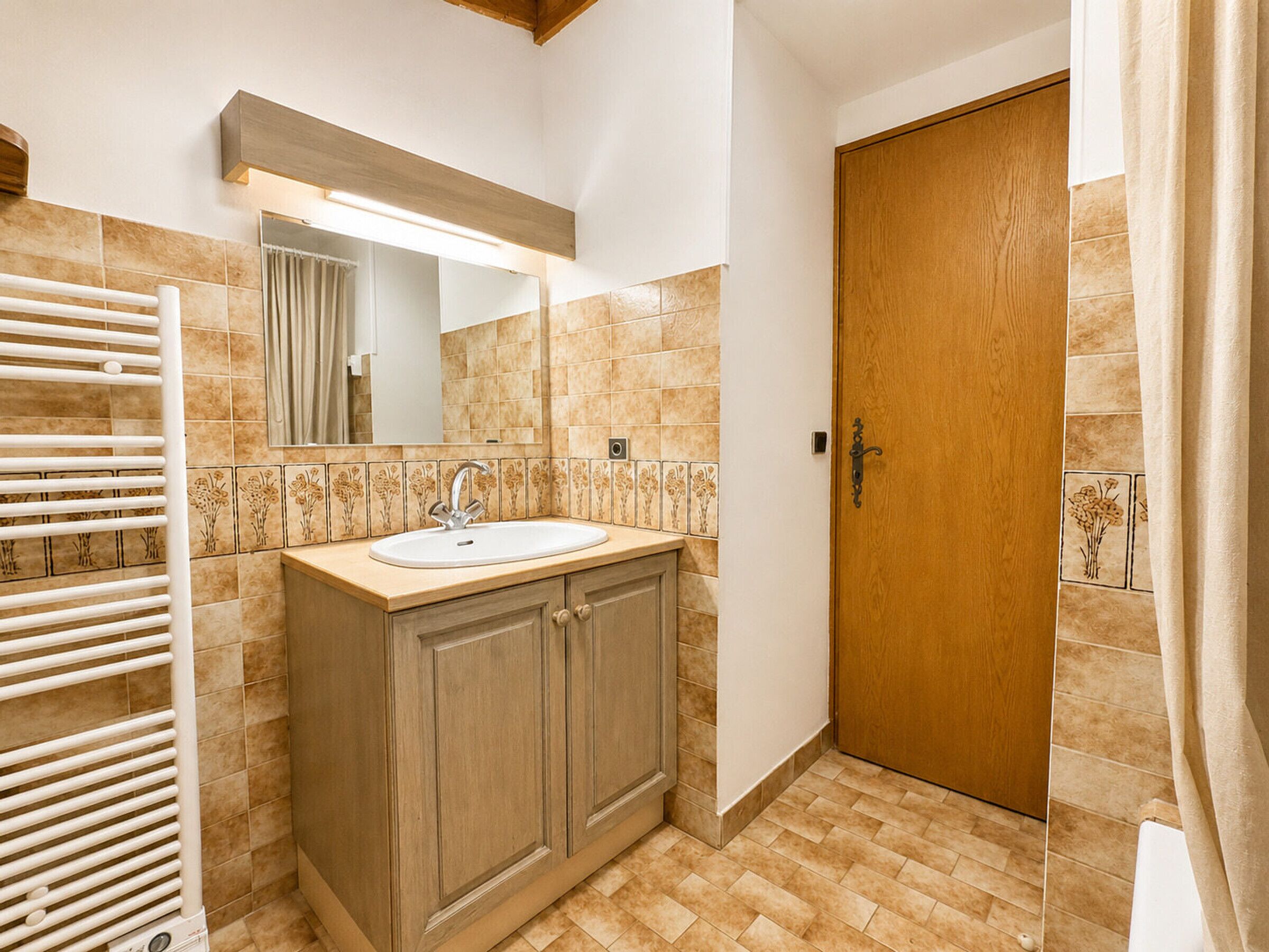 Un baño con lavamanos, espejo, toallero y puerta de madera.