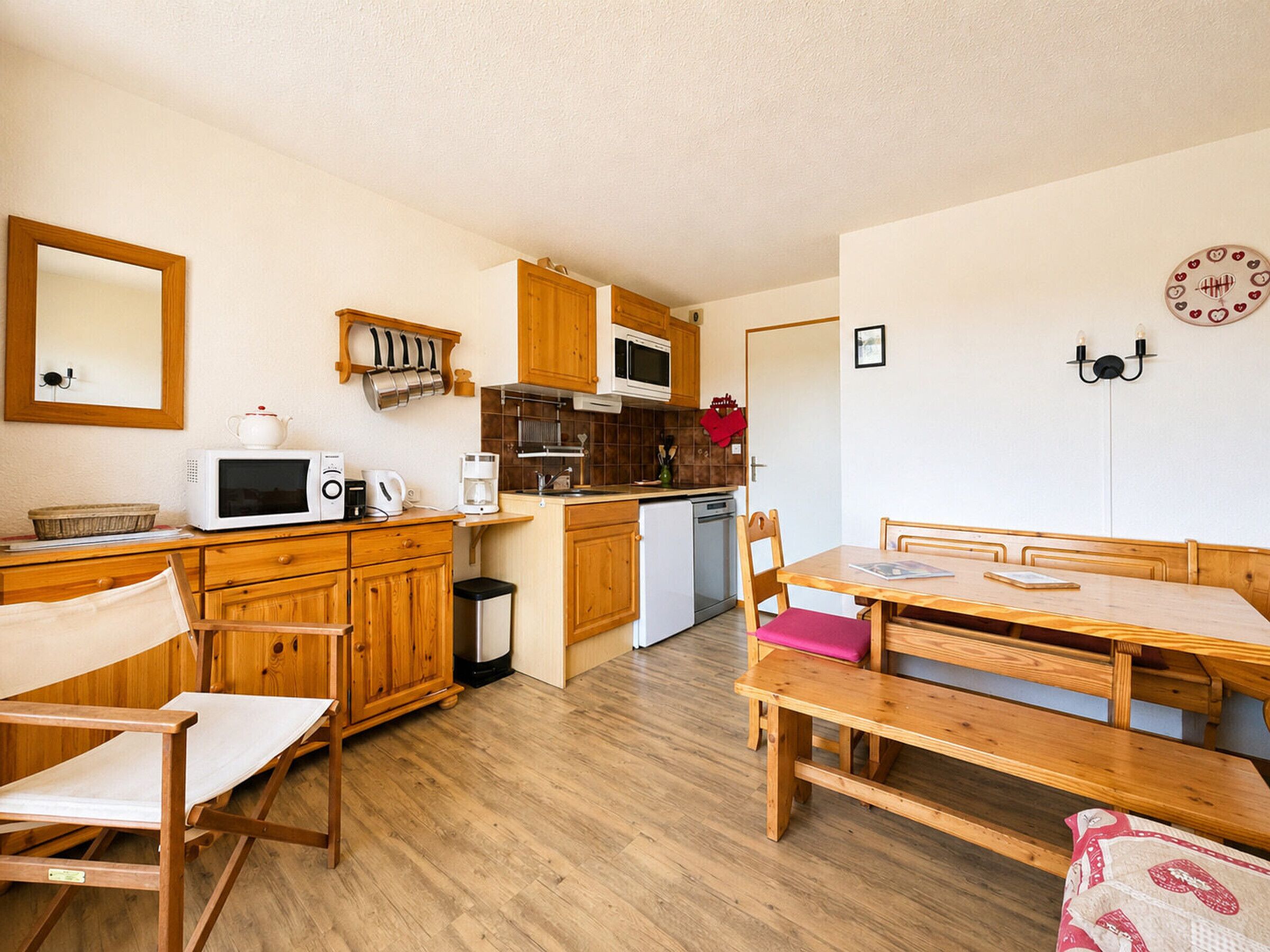 Cocina compacta con armarios de madera, microondas, lavamanos y un comedor con banco y sillas.