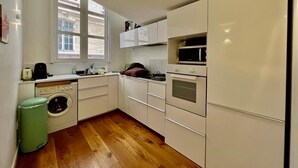 Cozinha compacta com armários brancos, máquina de lavar e janela que oferece luz natural.