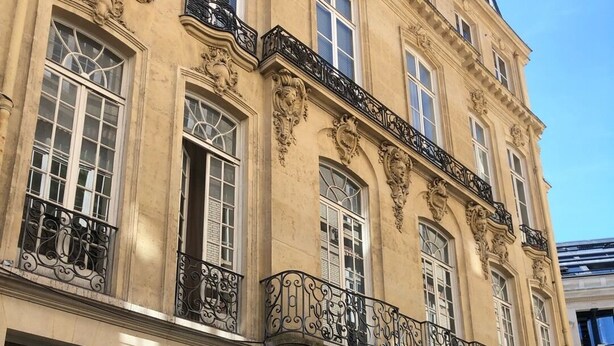 Um edifício histórico com varandas ornamentadas, grandes janelas e uma porta azul destacada.