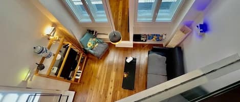 A high-ceilinged room with a wooden floor, a sofa, a small table, and a lamp.