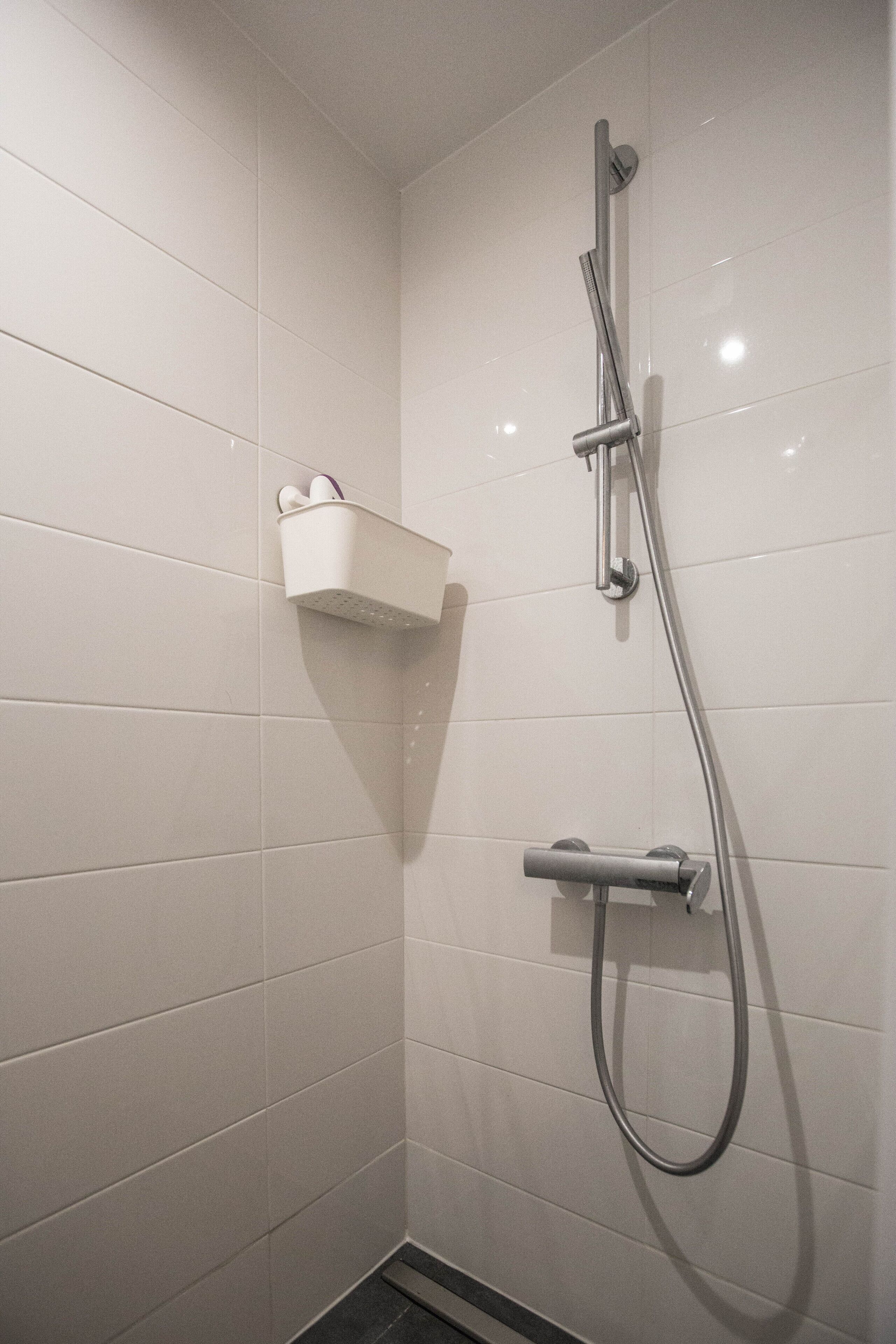 A shower with a handheld showerhead and a wall-mounted faucet.