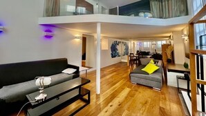 Uma sala de estar ampla com teto alto, um sofá, uma mesa de centro e um espaço de jantar com cadeiras.