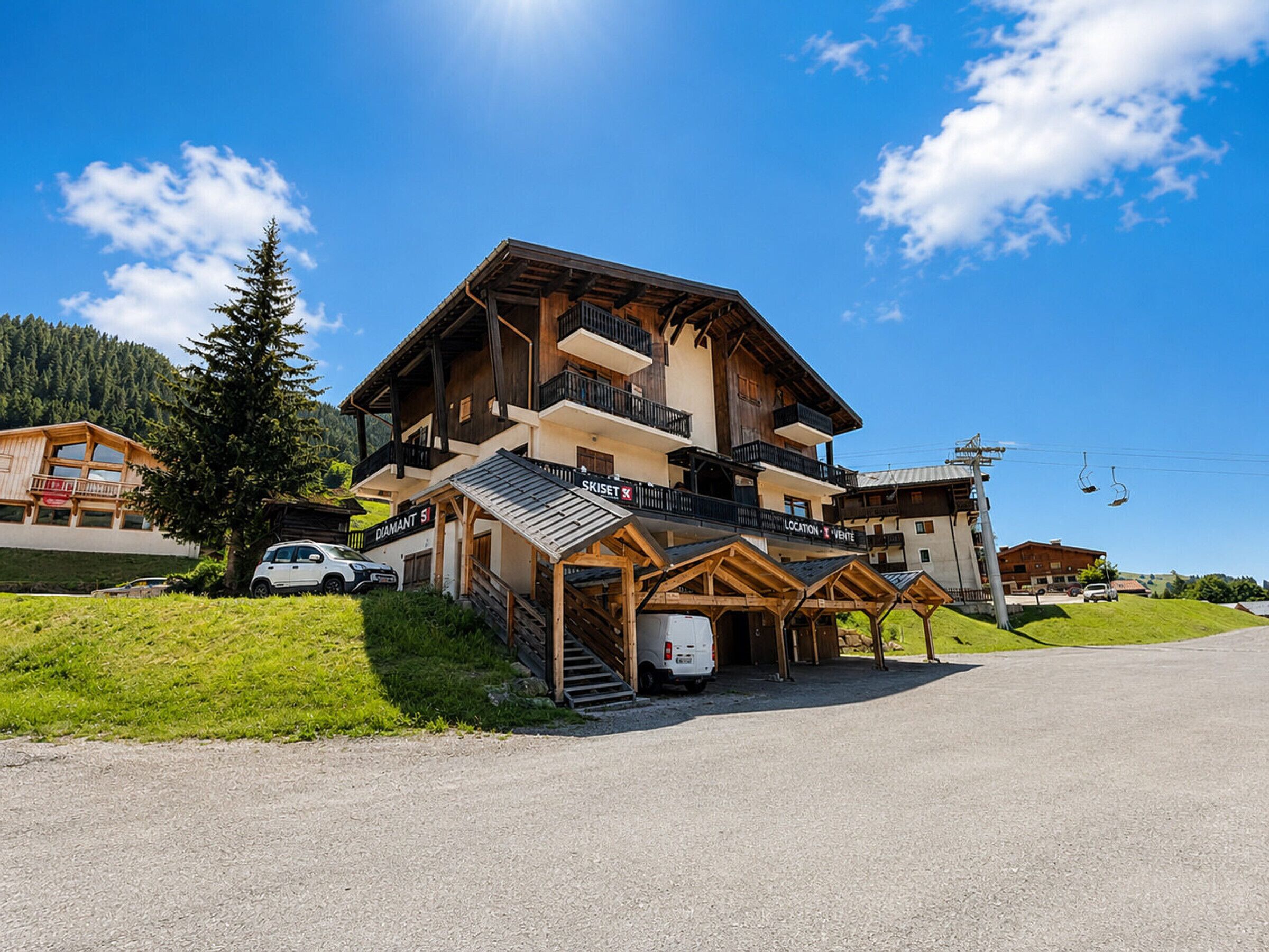 A multi-story wooden building with balconies, a ski lift in the background, and a clear sky.