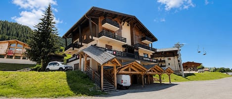 A multi-story wooden building with balconies, a ski lift in the background, and a clear sky.