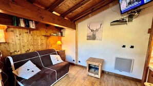 Una habitación acogedora con un sofá marrón, una mesita con una lámpara, un televisor en la pared y un cuadro con un ciervo.