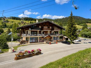 A two-story building with a ski lift in the background, a sign for 'DIAMANT SPORTS', and a wooden bench with flowers in the foreground.