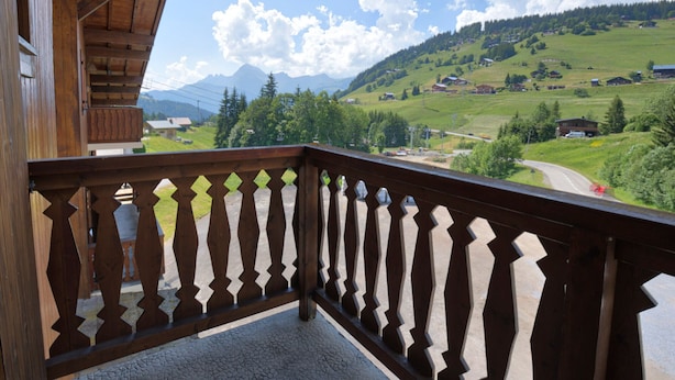 Un balcón de madera con vista a un valle verde y montañas.