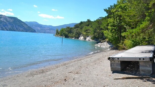A beach with a concrete structure, likely a boat ramp, and a clear view of a lake surrounded by mountains. - A corner of paradise: access lake side with exceptional view (Chorges)