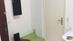 A small room with a green sofa, a wooden table, a white door, and a small white table with a magazine. - Studio old town 17m2, 1min from the sea (Menton)