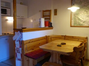 A compact kitchen with wooden cabinetry, a microwave, and a small dining area with a wooden table and bench.