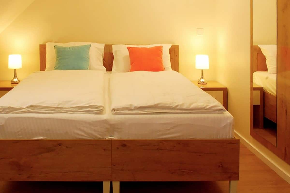 Ein Doppelbett mit zwei Nachttischen, jeweils mit einer Lampe, in einem Zimmer mit Holzboden und einem Holz-Kopfteil.