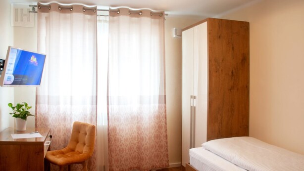 A bedroom with a bed, a desk with a chair, and a TV. - Hotel Isha (Frankfurt)