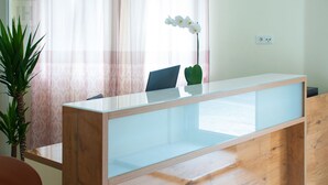 A reception desk with a glass top, a laptop, and a potted orchid. - Hotel Isha (Frankfurt)