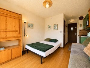 Una habitación compacta con una cama, un armario de madera, una lámpara de pie y una kitchenette.