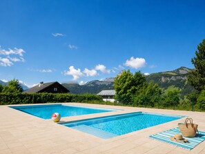 A swimming pool with a mountain backdrop, a house, and a picnic setup.