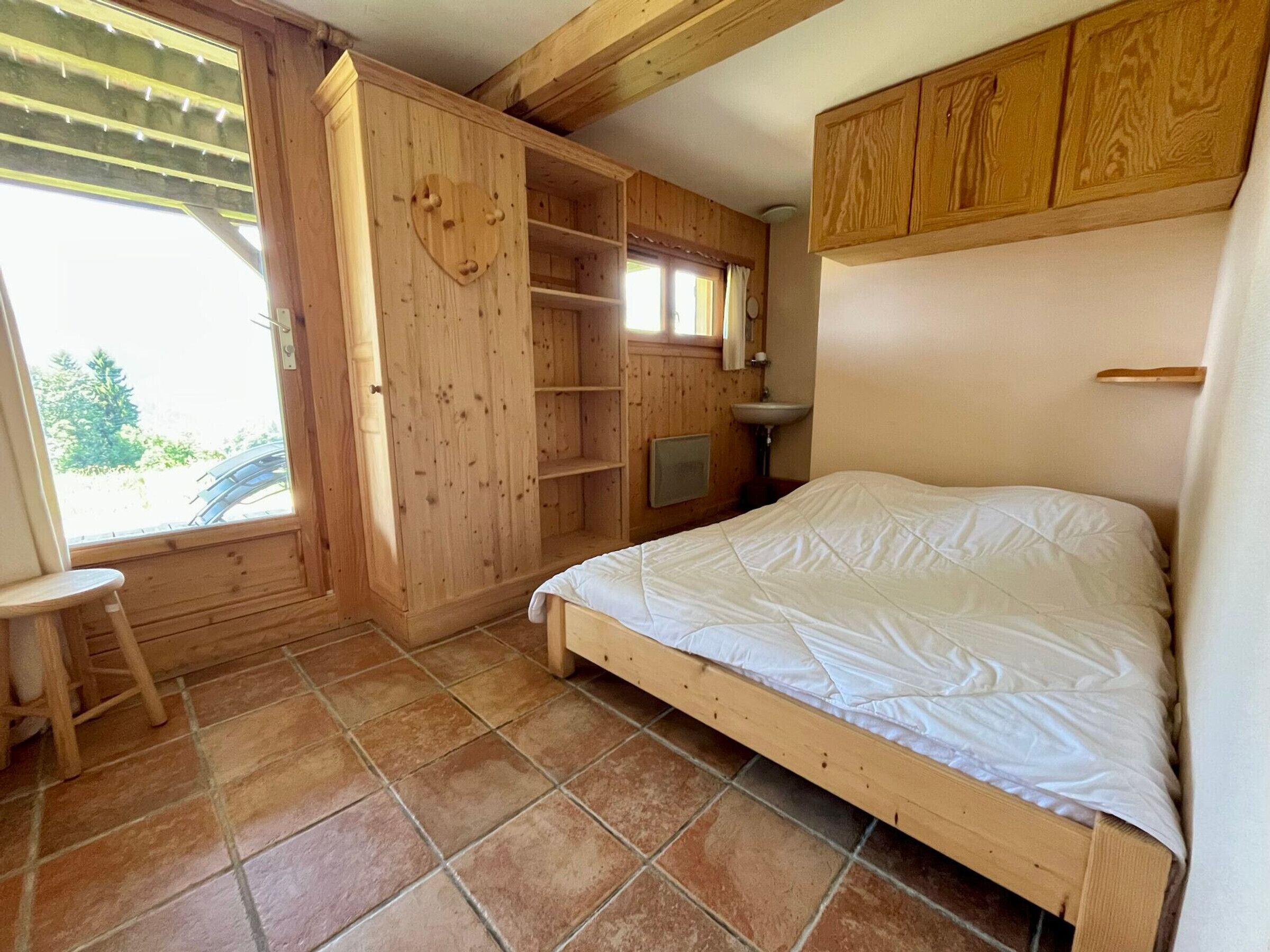 Un dormitorio con cama de madera, una mesita, armario empotrado y ventana con vistas al verdor.