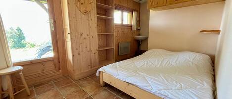 Un dormitorio con cama de madera, una mesita, armario empotrado y ventana con vistas al verdor.