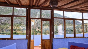 Una habitación con ventanas amplias, techo de madera, una mesa redonda y un sofá colorido.