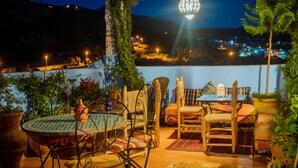 Un patio al aire libre con una mesa redonda, sillas y vistas a una ladera de noche.