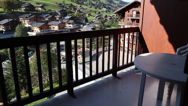 Un balcon donnant sur un village perché sur une colline, avec une table et une chaise.