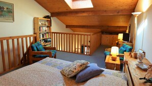 Une chambre confortable située sous les toits, avec un puits de lumière, une bibliothèque, un bureau avec une lampe et un téléviseur.