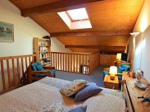 A cozy attic bedroom with a skylight, a bookshelf, a desk with a lamp, and a television.