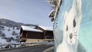 Un bâtiment en bois, doté d’un toit en pente recouvert de neige, situé sur une route enneigée, avec une montagne en arrière-plan.