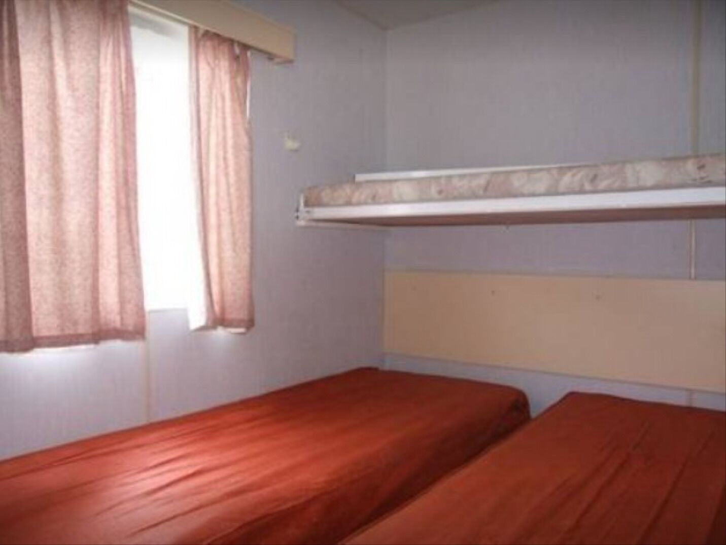 Une chambre avec deux lits simples, une fenêtre avec des rideaux et un lit superposé au-dessus.