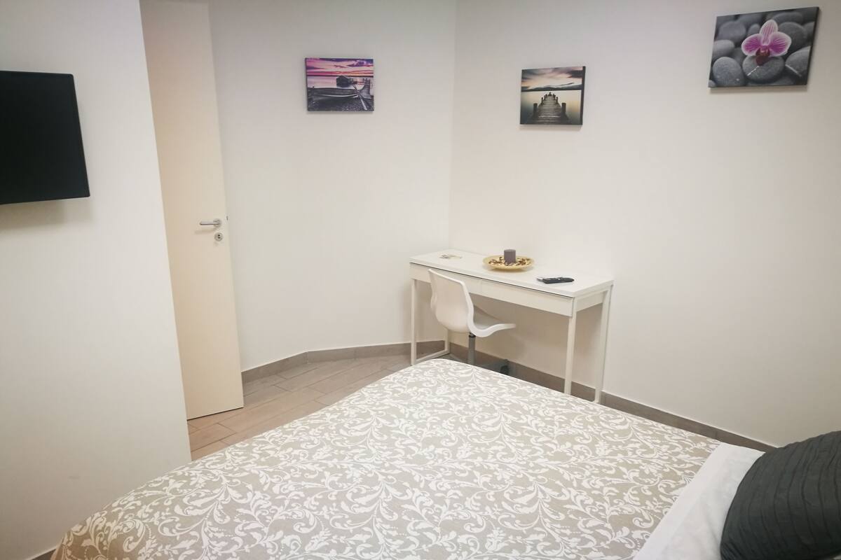 A bedroom with a bed, a desk, and two wall-mounted pictures.