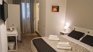 A hotel room with a bed, a desk with a TV, a nightstand with a lamp, and a window with curtains. - 'O Vic' Stritt (Naples)