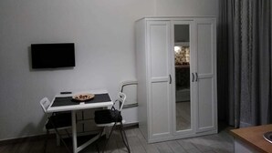 A compact room with a dining table, chairs, a TV mounted on the wall, and a wardrobe with a mirror. - 'O Vic' Stritt (Naples)