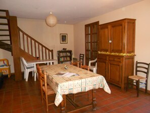 A dining area with a table set for four, surrounded by wooden chairs. A staircase is visible to the left, and a wooden cabinet with glass doors is to the right.
