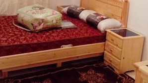 A bedroom with a wooden bed, a bedside table, a nightstand, a floral-patterned pillow, a rolled-up blanket, and a dark patterned rug. - pretty apt near beach and cornice (Al Hoceïma)