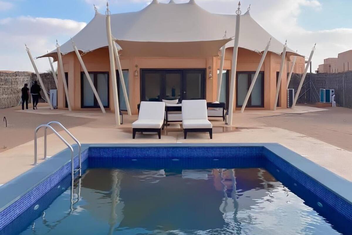Piscina con sillones de descanso y una zona de estar techada.