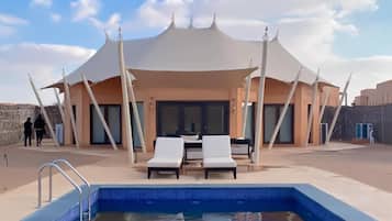 Piscina con sillones de descanso y una zona de estar techada.