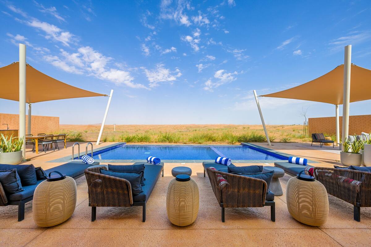 Zona de piscina con sillones reclinables, una piscina y un paisaje desértico al fondo.