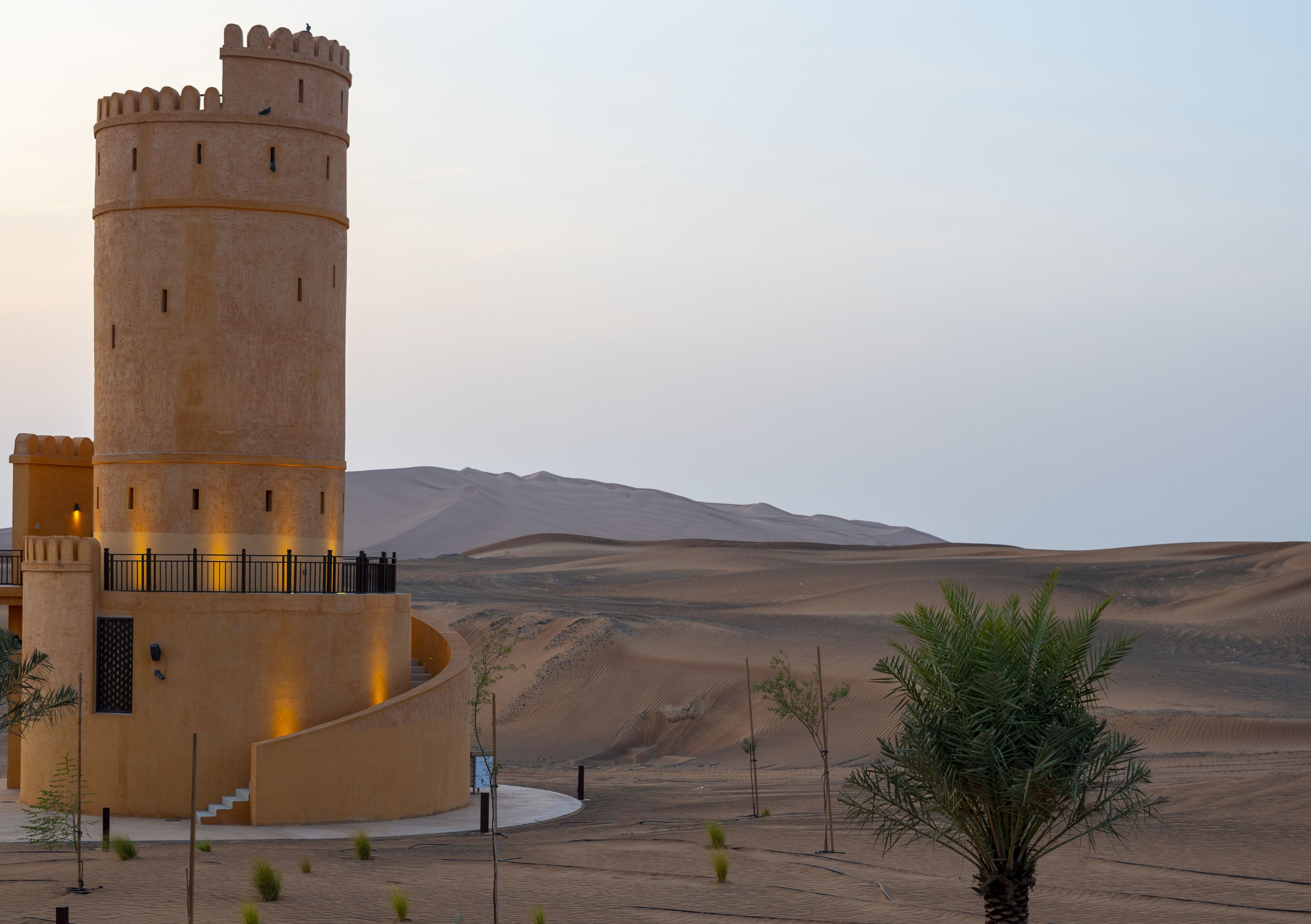A tower with a spiral staircase, surrounded by sand dunes and sparse vegetation.