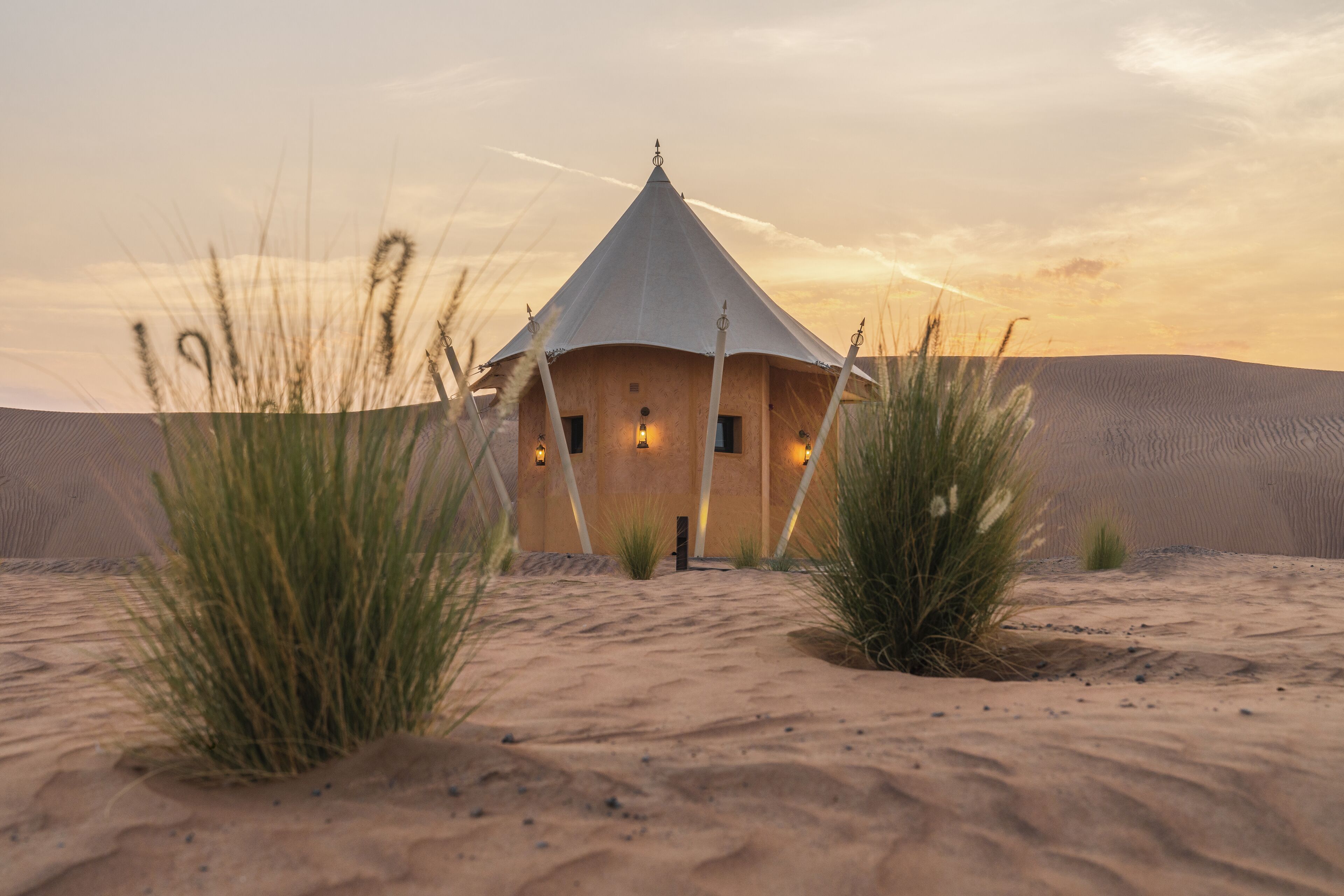 Une construction située dans le désert, dotée d’un toit conique et entourée de dunes de sable et d’une végétation clairsemée.