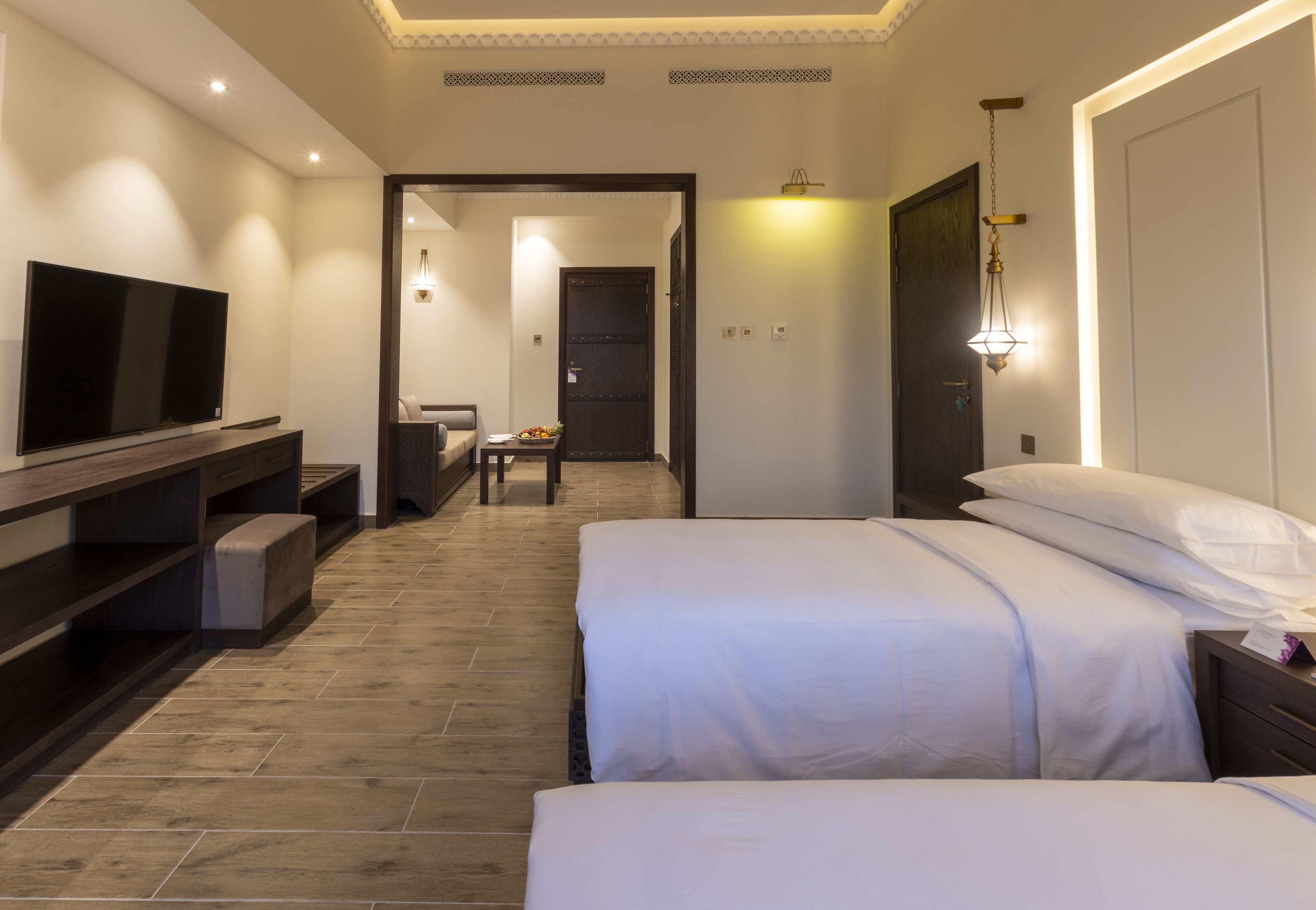 A hotel room with two beds, a TV, a desk, and a bathroom visible through an open door.