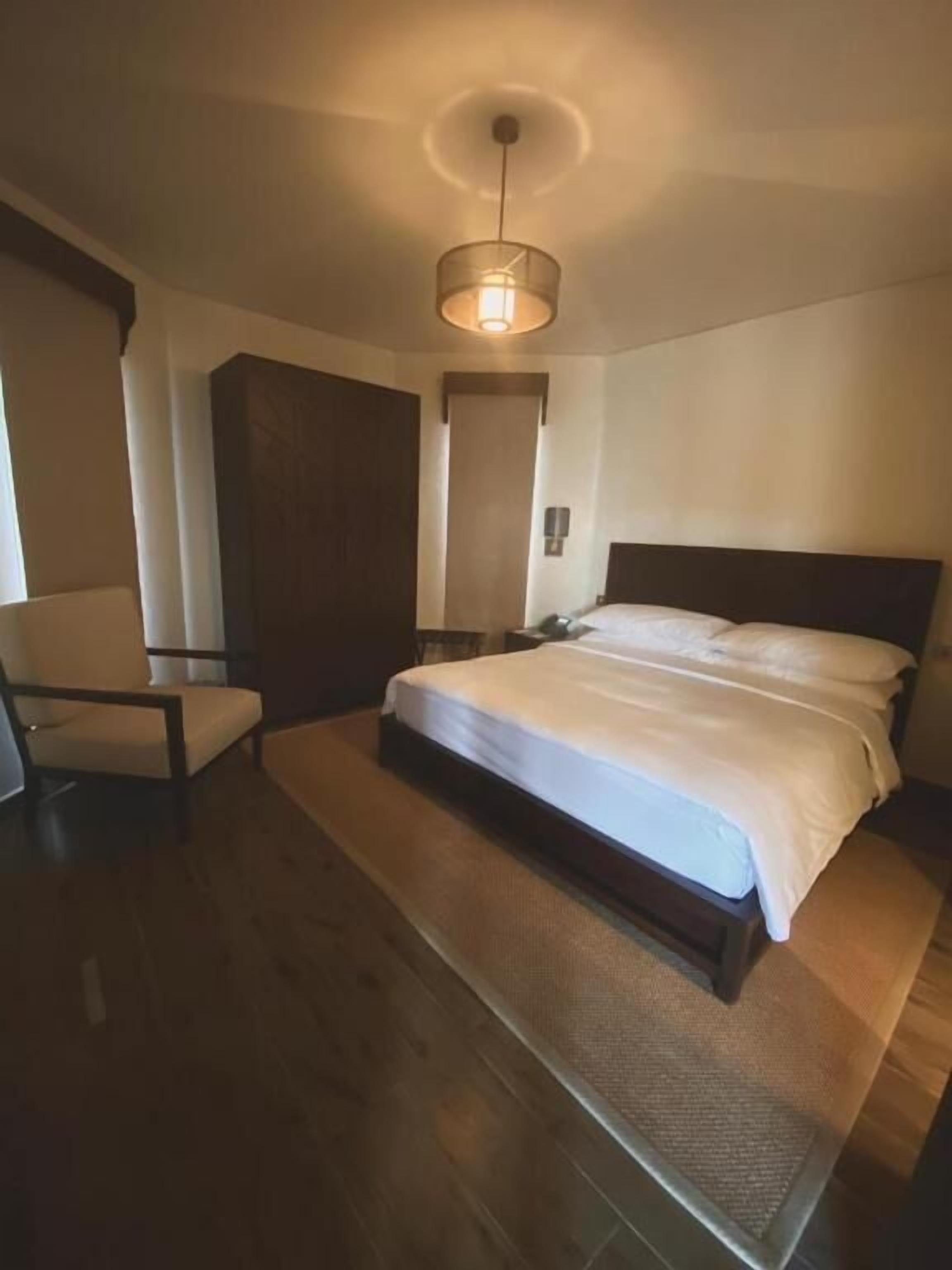 Ein Hotelzimmer mit einem großen Bett, einem Sessel, einem Kleiderschrank und einer Deckenleuchte.