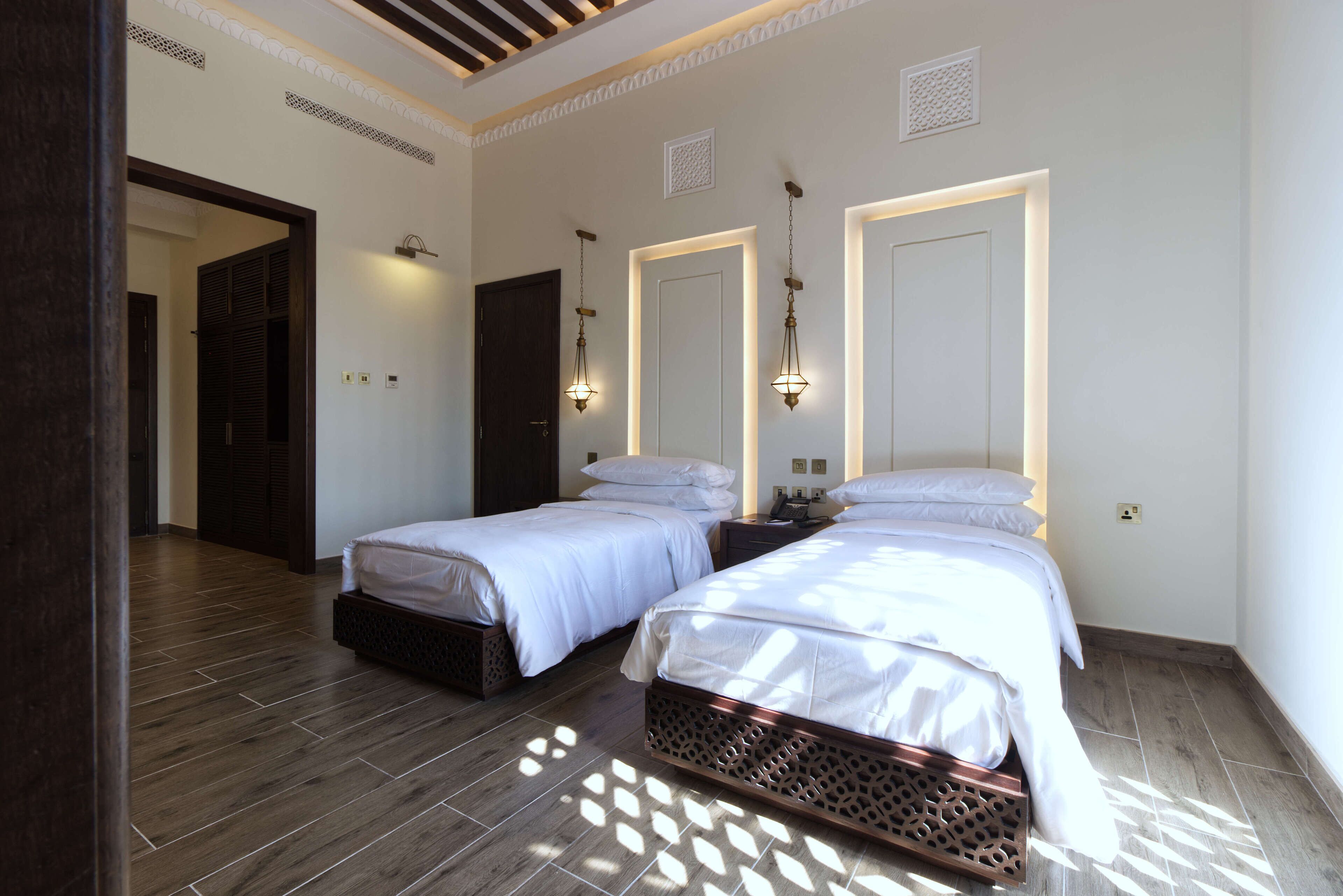 Habitación de hotel con dos camas, piso de madera y techo decorativo.