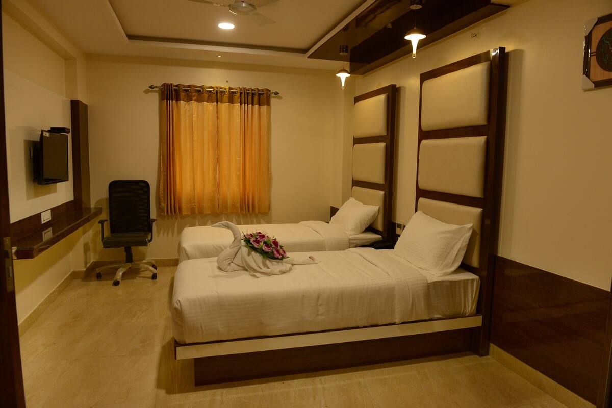 A hotel room with two beds, a TV, a desk, and a chair.