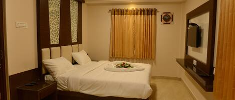 Habitación de hotel con cama, mesita de noche, televisor y ventilador de techo.
