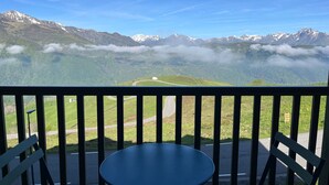 A balcony with a table and chairs overlooking a mountainous landscape with a winding road and a small building. - Spacious Apt for 6 with Balcony in Peyragudes, 500m from Slopes, Free Spa Access (Peyragudes)
