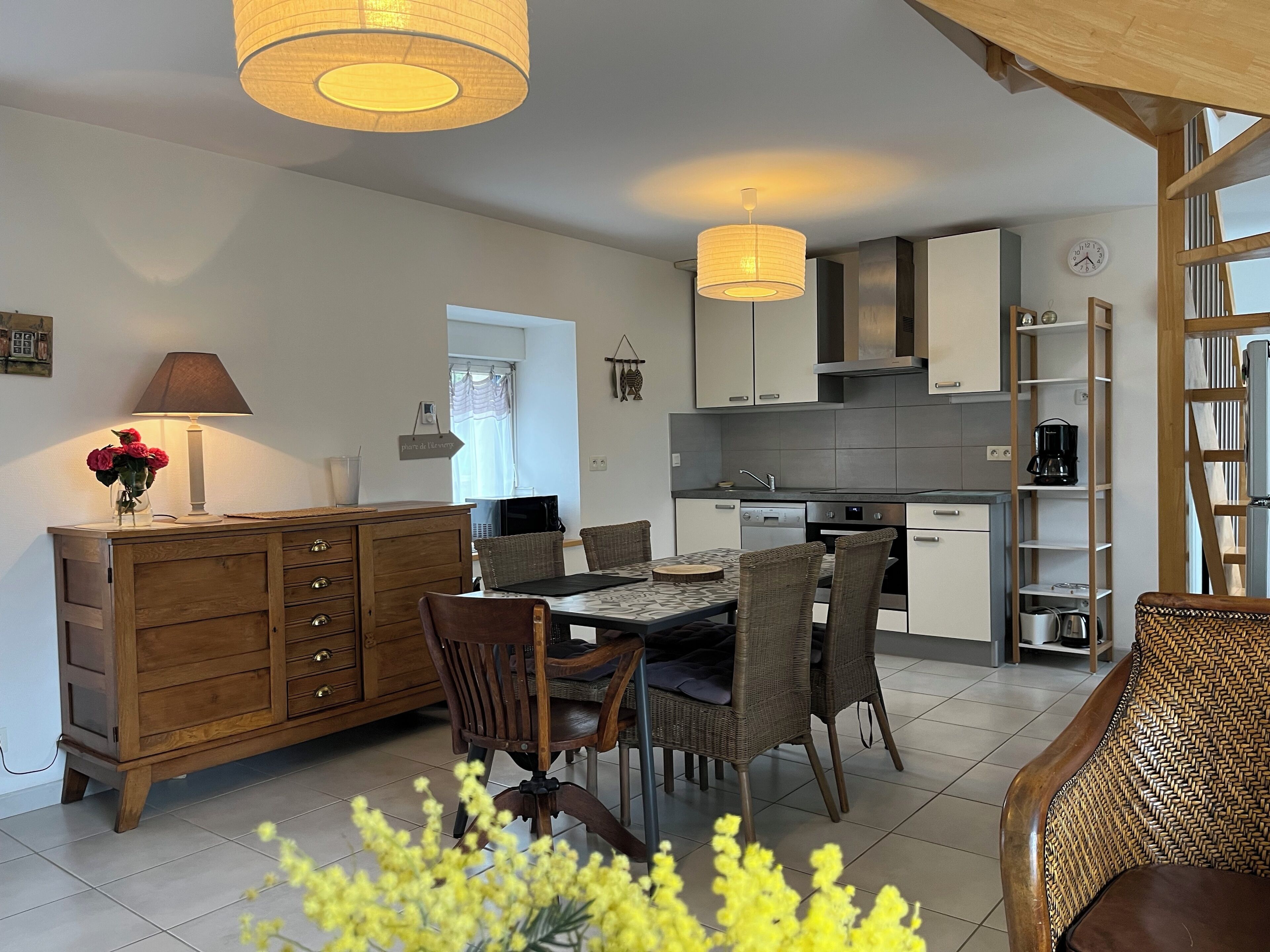 A modern kitchen with white cabinets, a dining area with wicker chairs, and a wooden dresser.