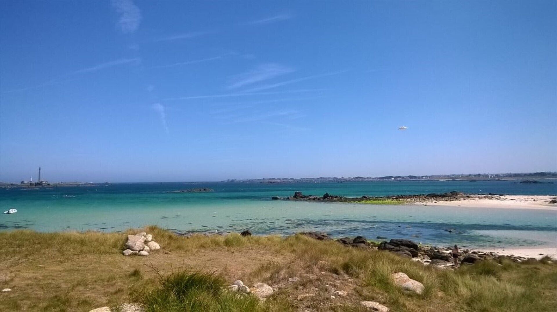Un paisaje costero con cielo despejado, una playa de arena y afloramientos rocosos.